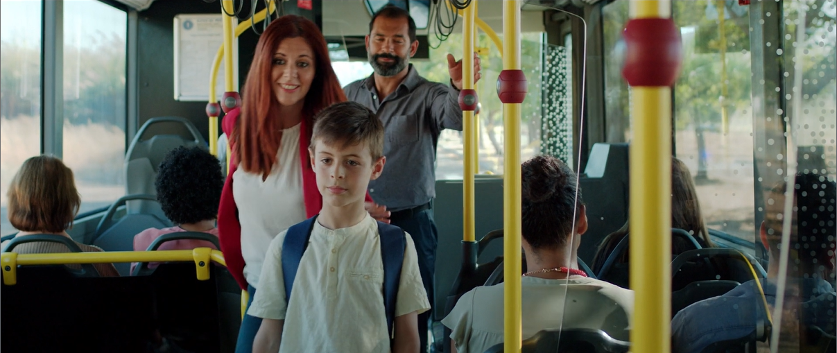 interior de autocarro com mulher, homem e criança no corredor entre as cadeiras. várias pessoas sentadas.