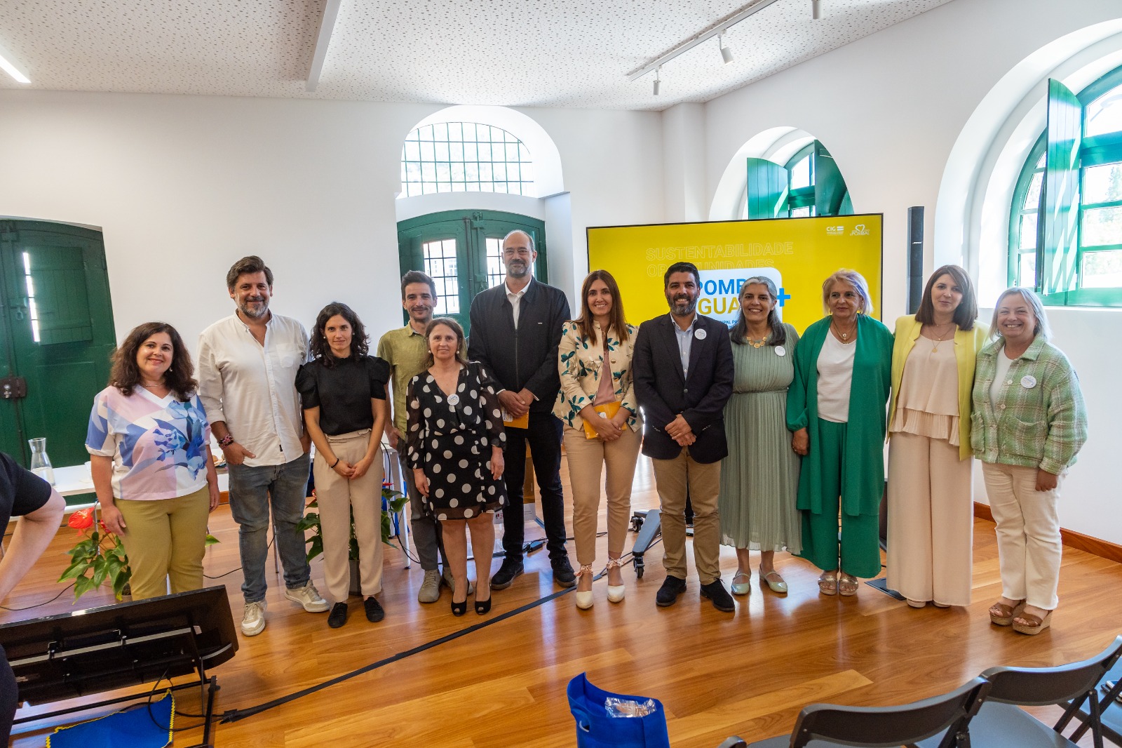 Várias pessoas numa sala posam em frente a um cartaz Pombal + Igual