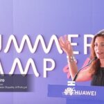 Presidente da CIG, Sandra Ribeiro, fala num púlpito. Em fundo, parede lilás com referência Summer Camp