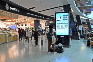 Cartaz afixado num mupi no aeroporto com uma mulher negra a olhar e outras pessoas a passar