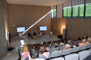 Fotografia com grande plano do auditório, com o público de costas e os oradores ao fundo