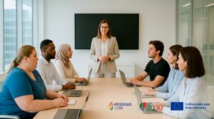 A fotografia de uma reunião de trabalho, seis pessoas sentadas à volta de uma mesa com computadores portáteis, uma mulher de pé, ao centro, conduz a reunião-