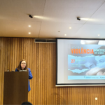 presidente da cig, carina quaresma discursa em púlpito. em fundo, tela de projeção: seminário violência doméstica e de género. 27 de março