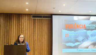 presidente da cig, carina quaresma discursa em púlpito. em fundo, tela de projeção: seminário violência doméstica e de género. 27 de março