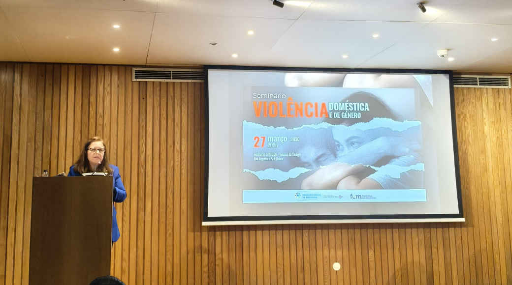 presidente da cig, carina quaresma discursa em púlpito. em fundo, tela de projeção: seminário violência doméstica e de género. 27 de março